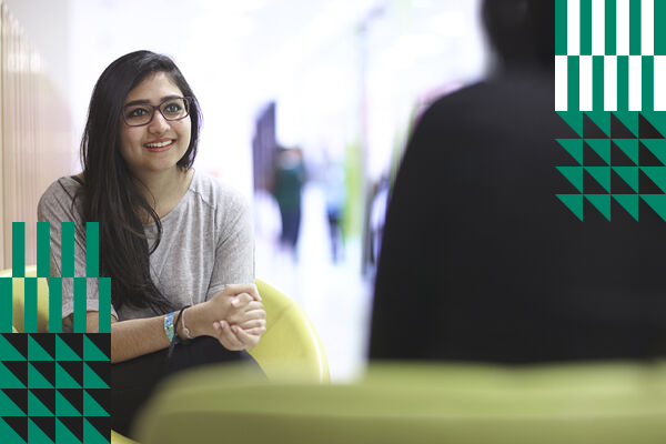 Female student sat in green chair smiling at person facing her who has their back to the camera